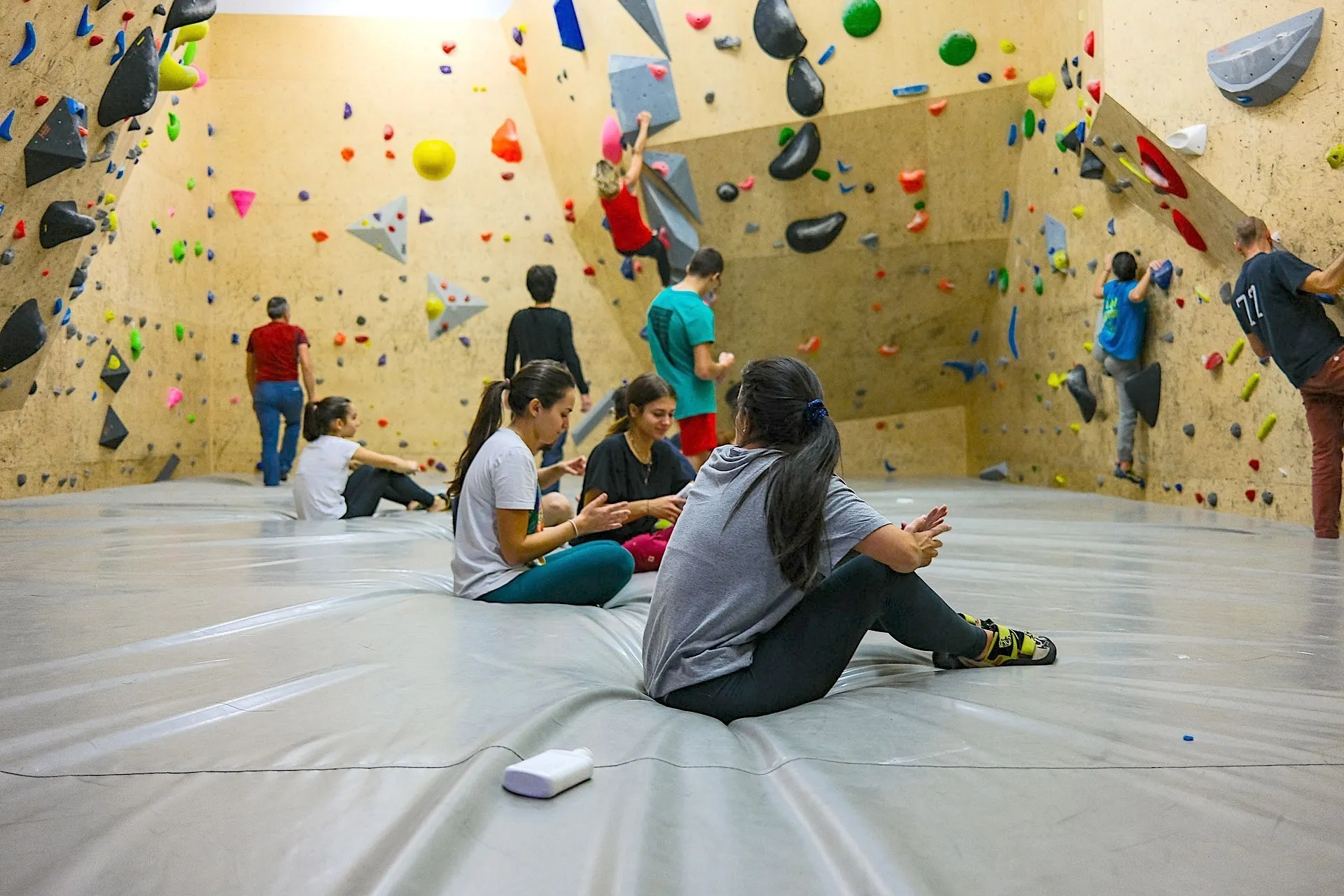 La sala boulder: alcune ragazze chiacchierano sedute sul grande materasso mentre altri arrampicano sulle pareti piene di prese colorate